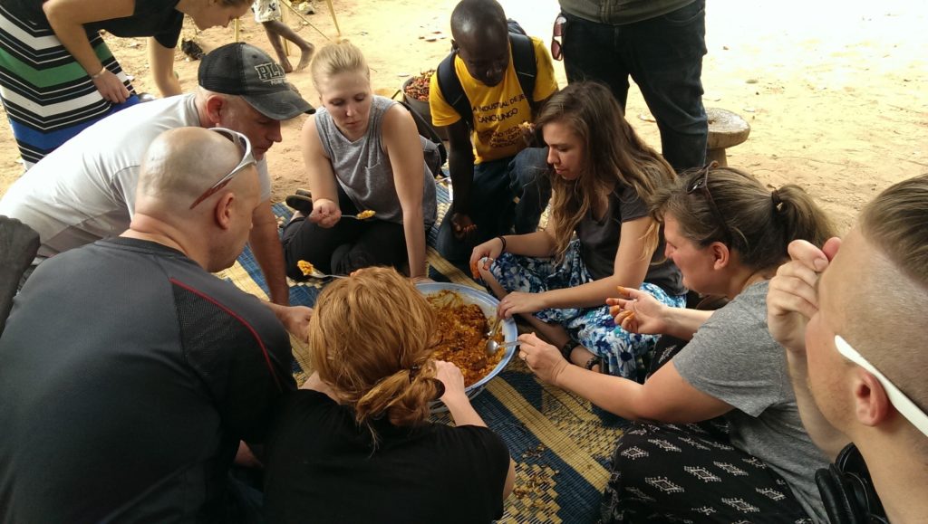 Tourists in Guinea-Bissau eating a traditional meal with locals. 